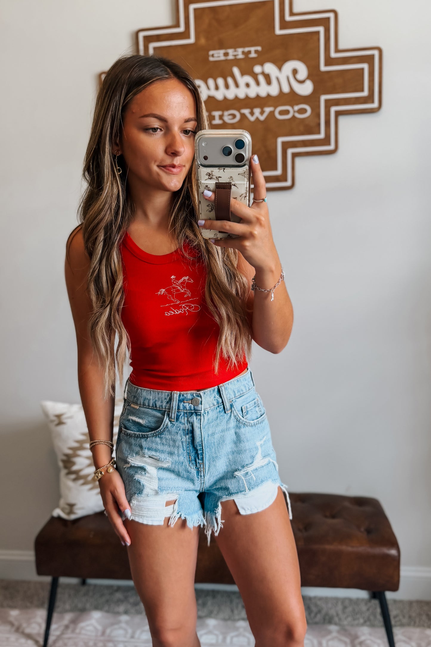 Model wearing high-rise light wash distressed denim cutoff shorts styled with a western-inspired outfit for a casual summer look.