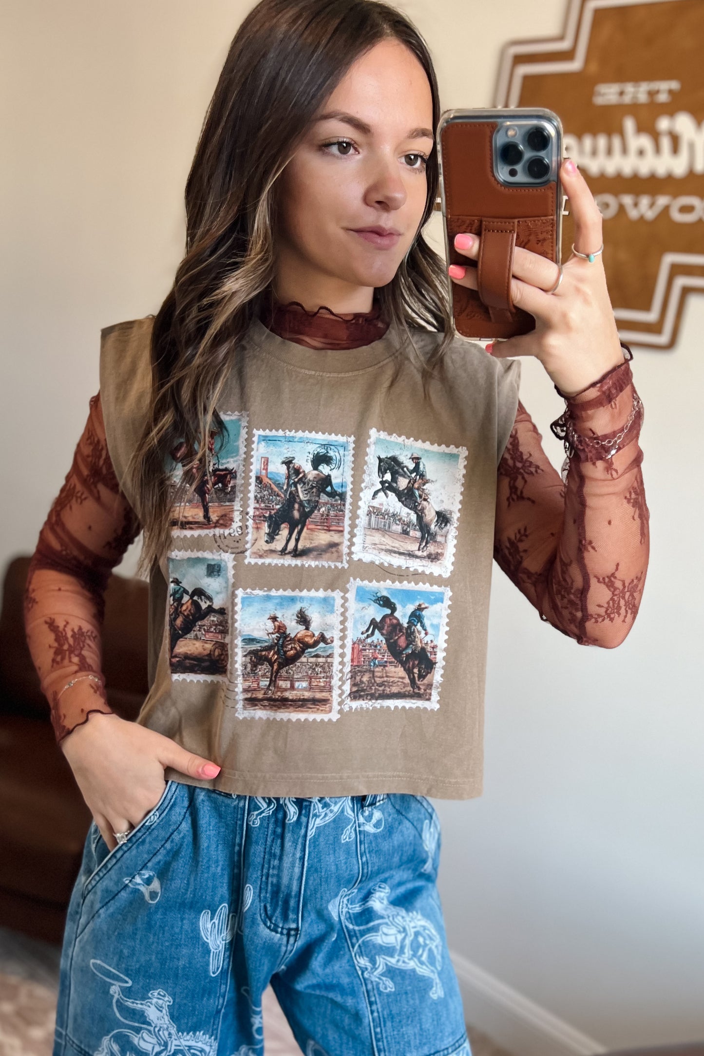 Sheer long-sleeve lace top in brown with floral pattern, featuring a high neckline and lightweight mesh fabric, layered under a western graphic muscle tank