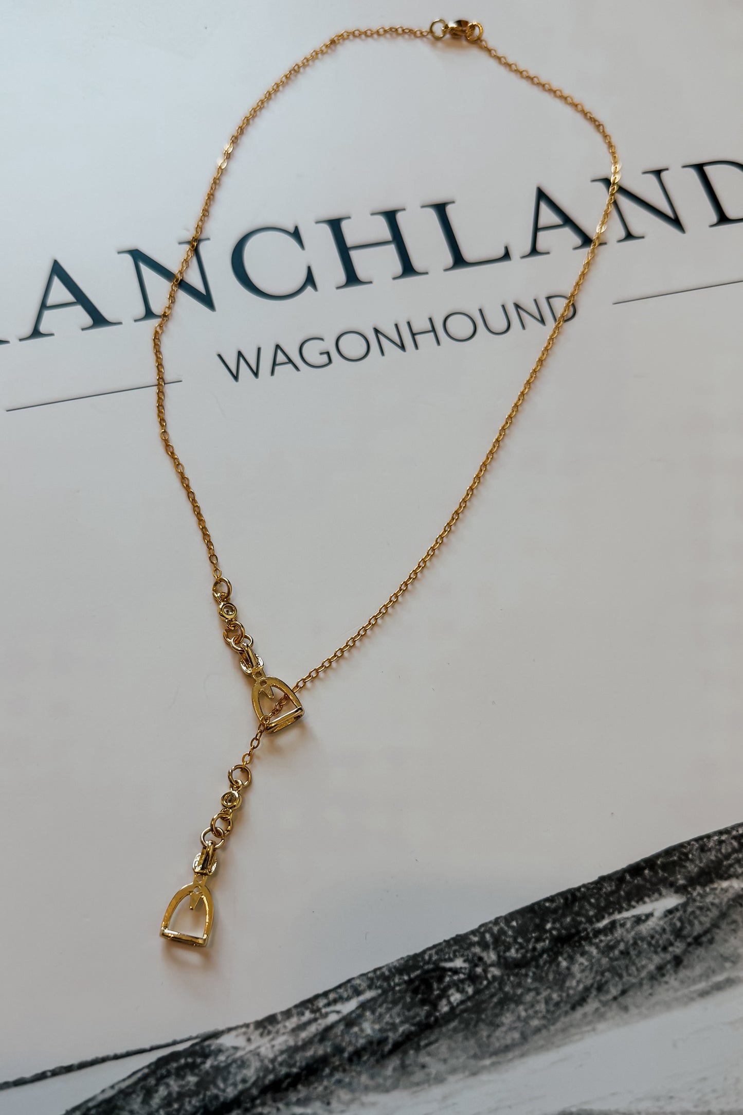 Close-up of gold stirrup lariat necklace showing dainty chain and slider detail.
