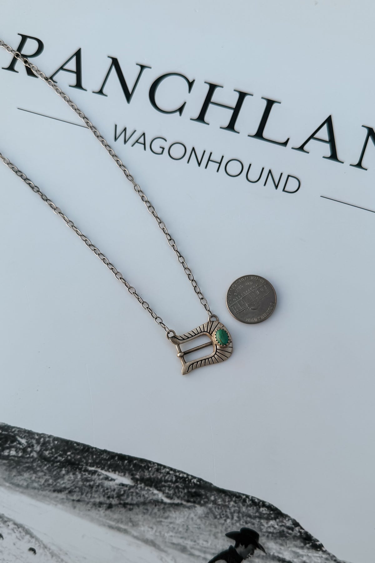 A silver-toned chain necklace with a small pendant featuring a green heart-shaped stone,