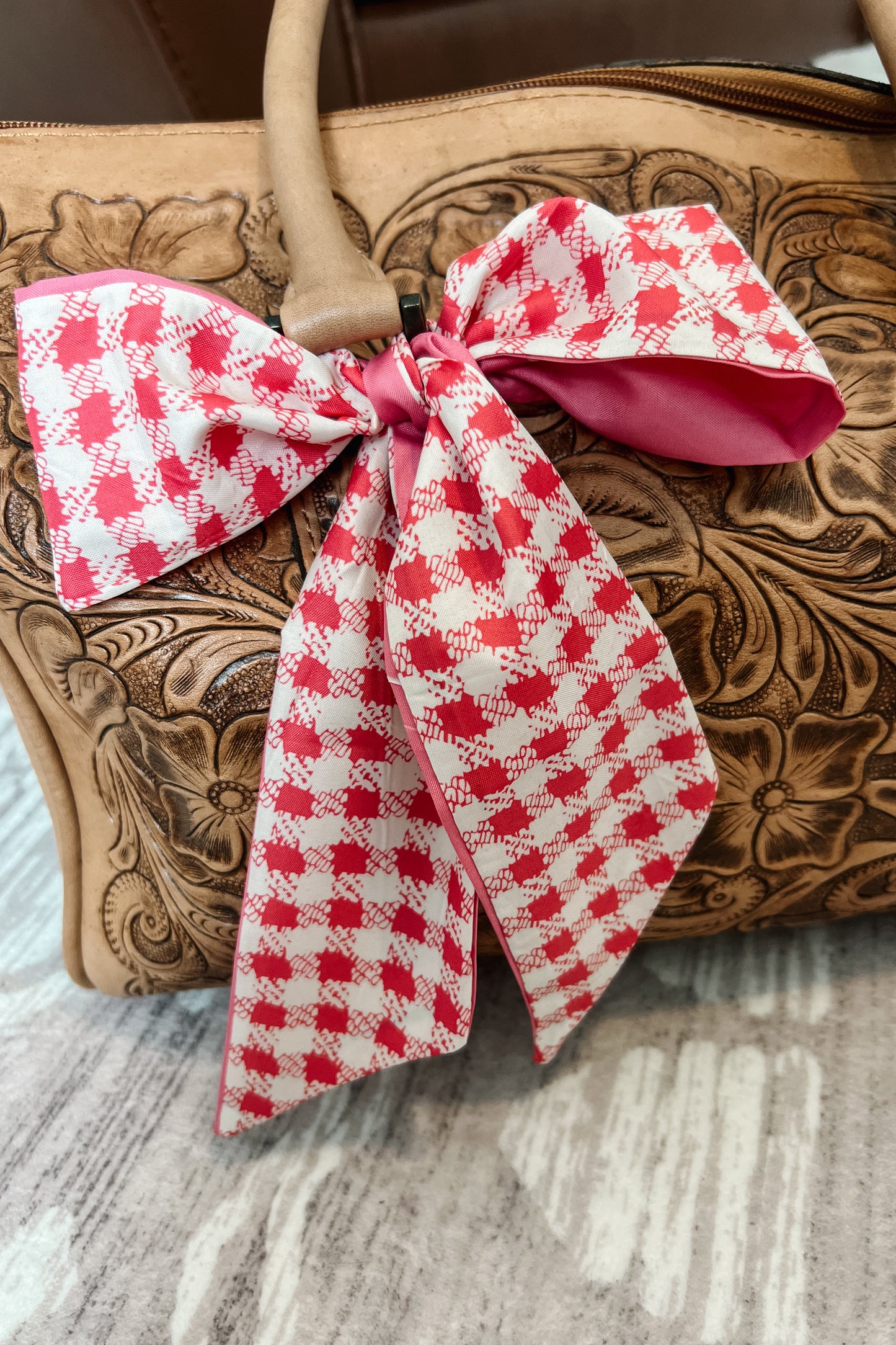 Pink and ivory checkered twilly scarf tied in bow around tooled leather purse handle.