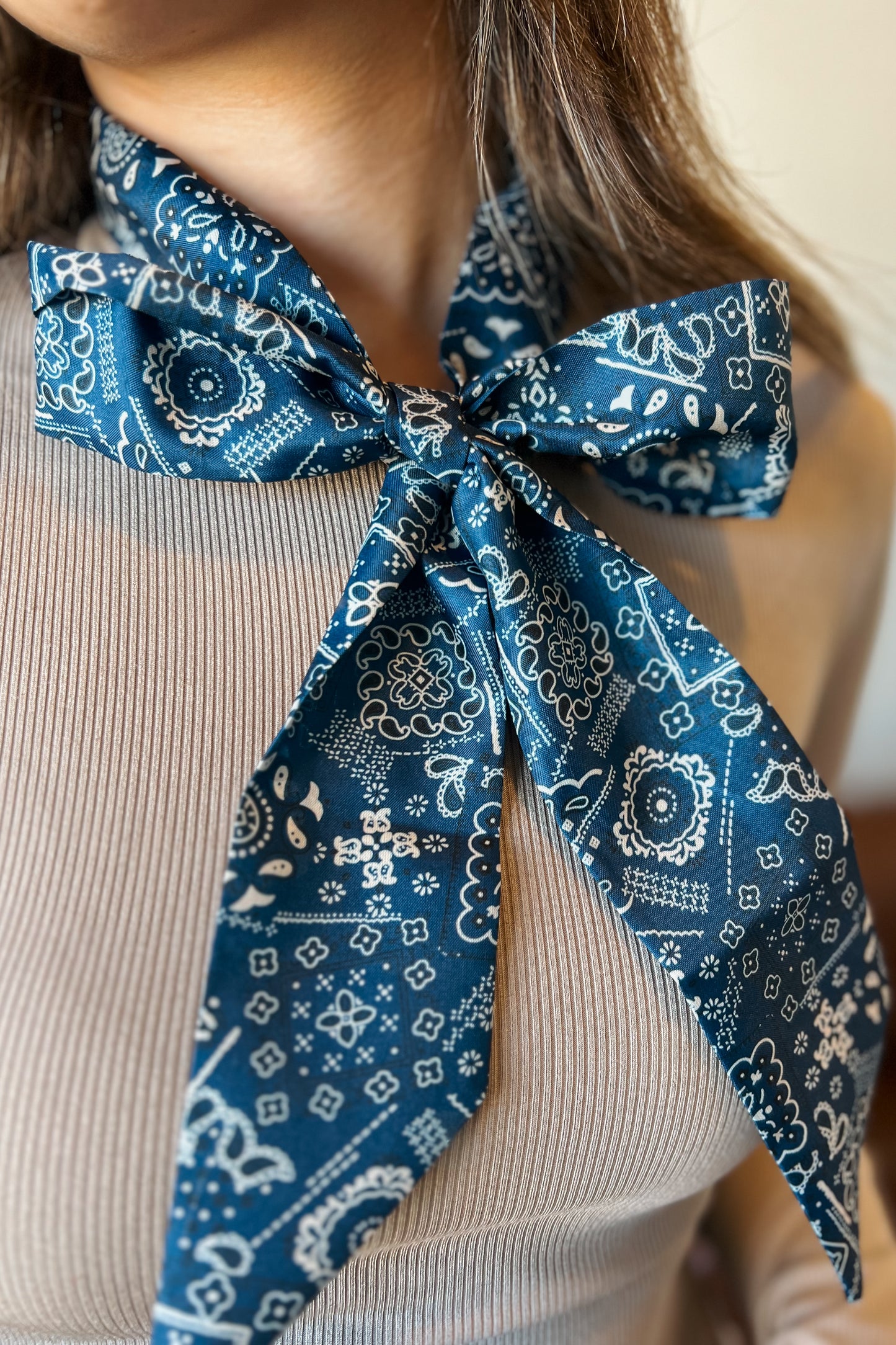 Close-up of a blue paisley bandana tied around the neck, featuring a white western-inspired print and pointed ends.
