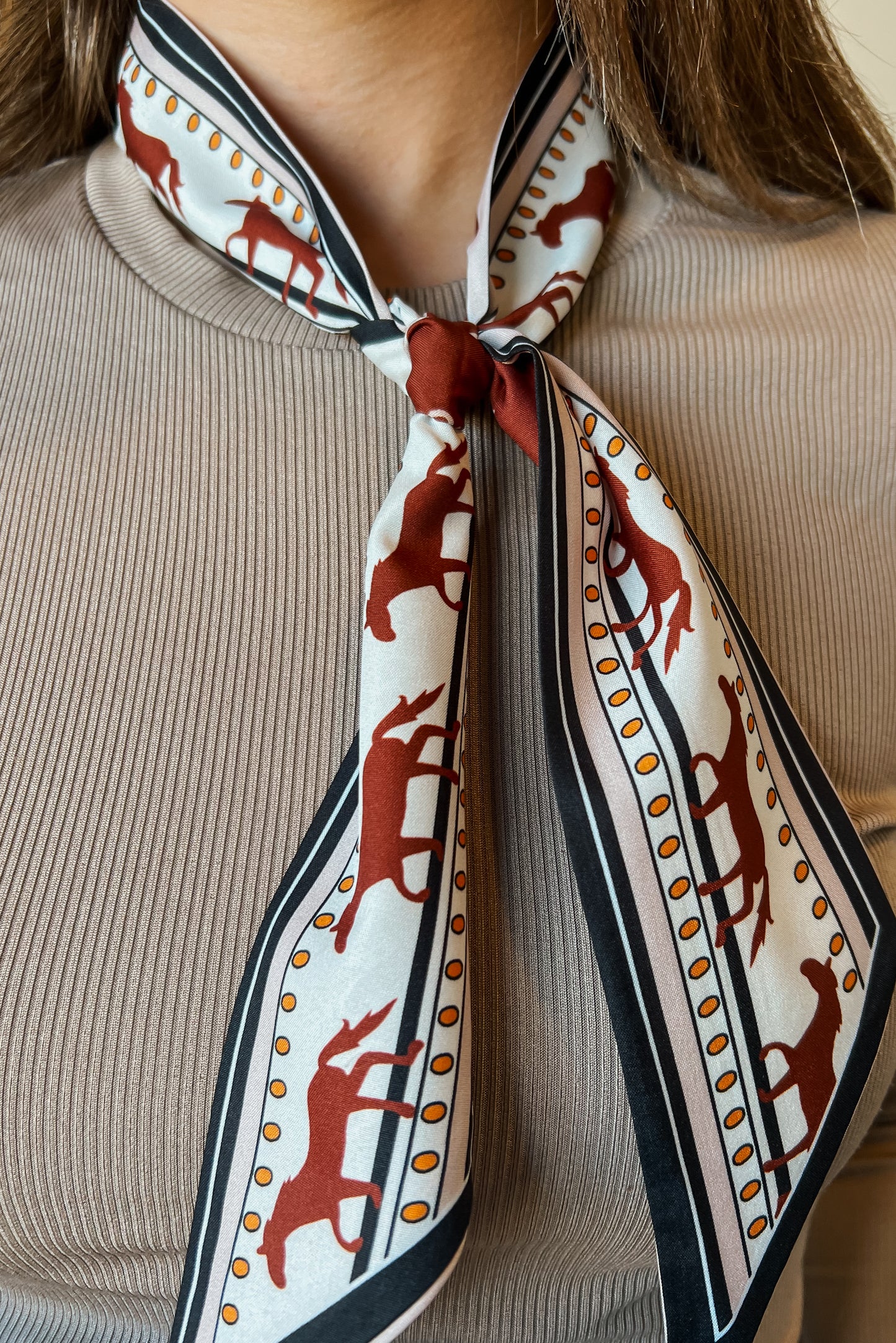 Western print neck scarf with rust horse motifs and black and cream border, tied at the neck.