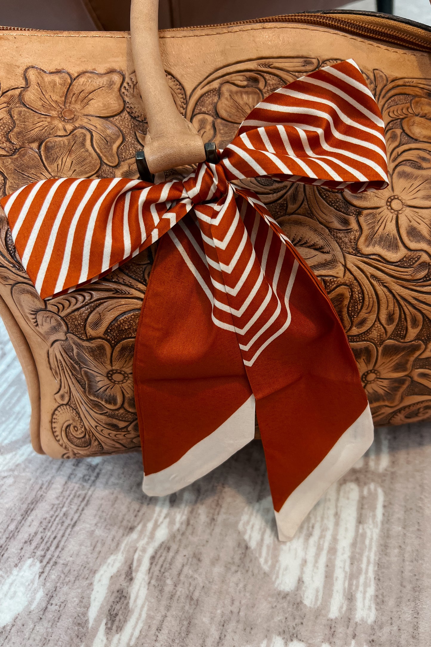 Rust and cream striped Twilly tied in a bow on tooled leather purse strap