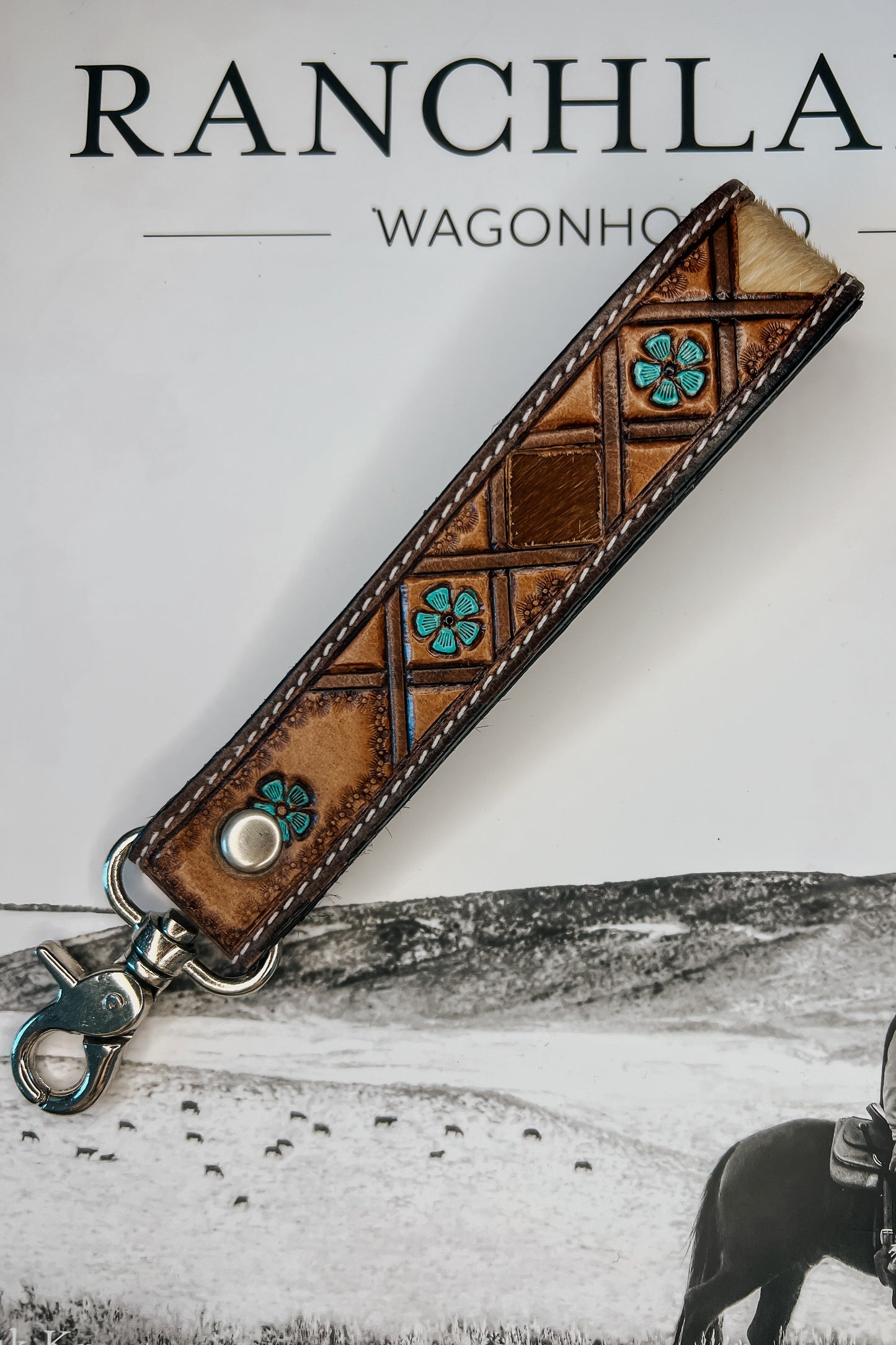 Brown leather wristlet keychain with hair-on cowhide inlay, turquoise accents, contrast stitching, and silver swivel clasp.
