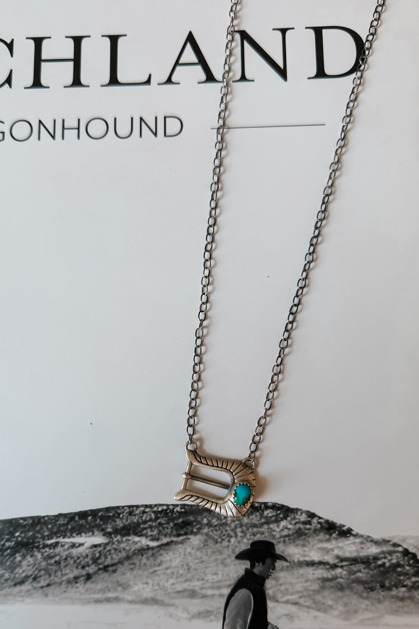 A silver-toned chain necklace with a western-style rectangular pendant featuring a turquoise accent,