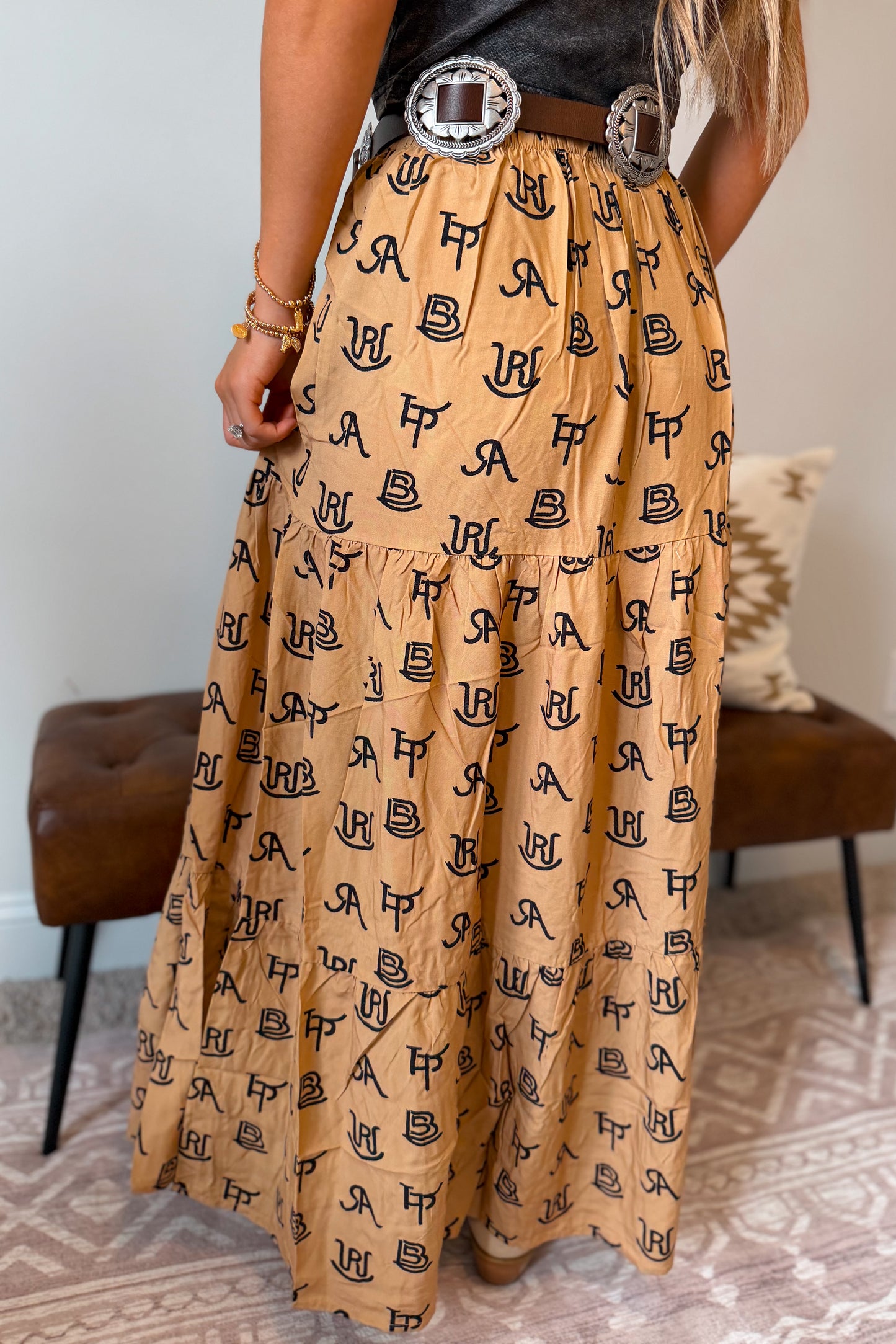 Back view of a tan maxi skirt with a black cattle brand pattern throughout. Features a stretchy elastic waistband and a relaxed, flowing fit.
