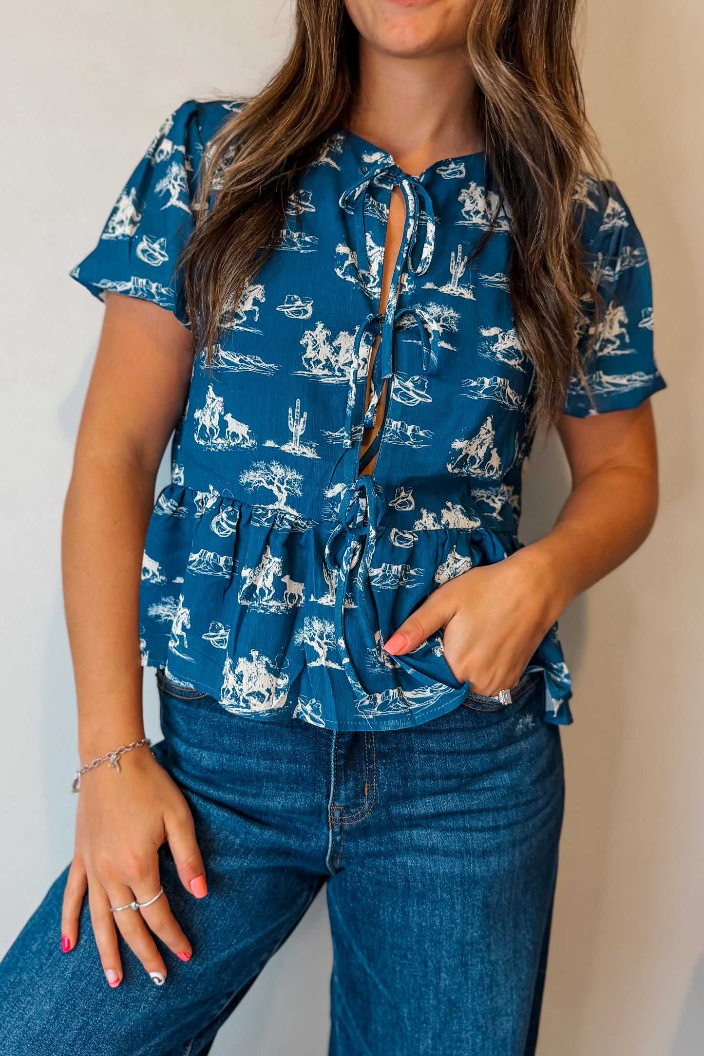 Blue puff sleeve babydoll top with white western print and front tie detail.