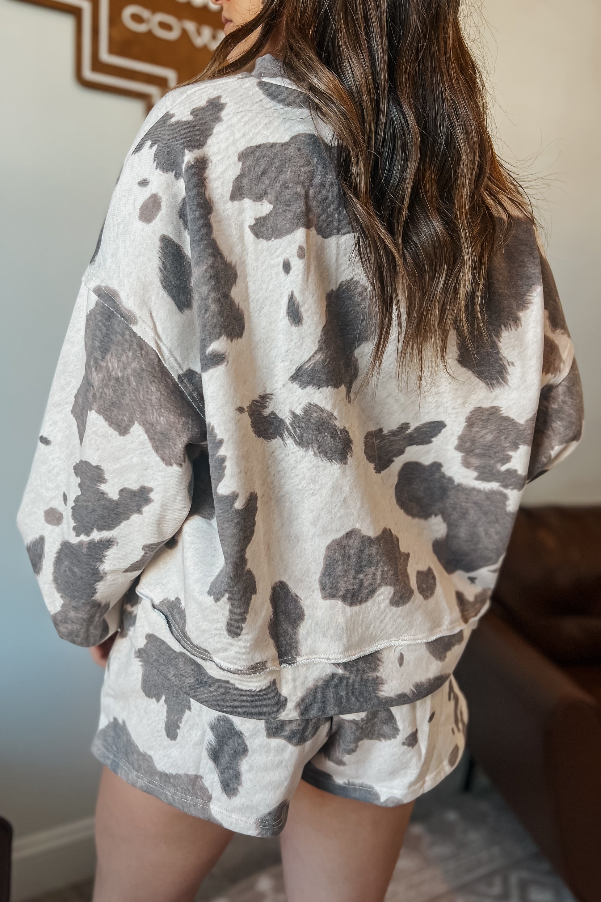 Back view of Gray and cream cow print lounge set featuring a long sleeve V-neck top and matching drawstring shorts