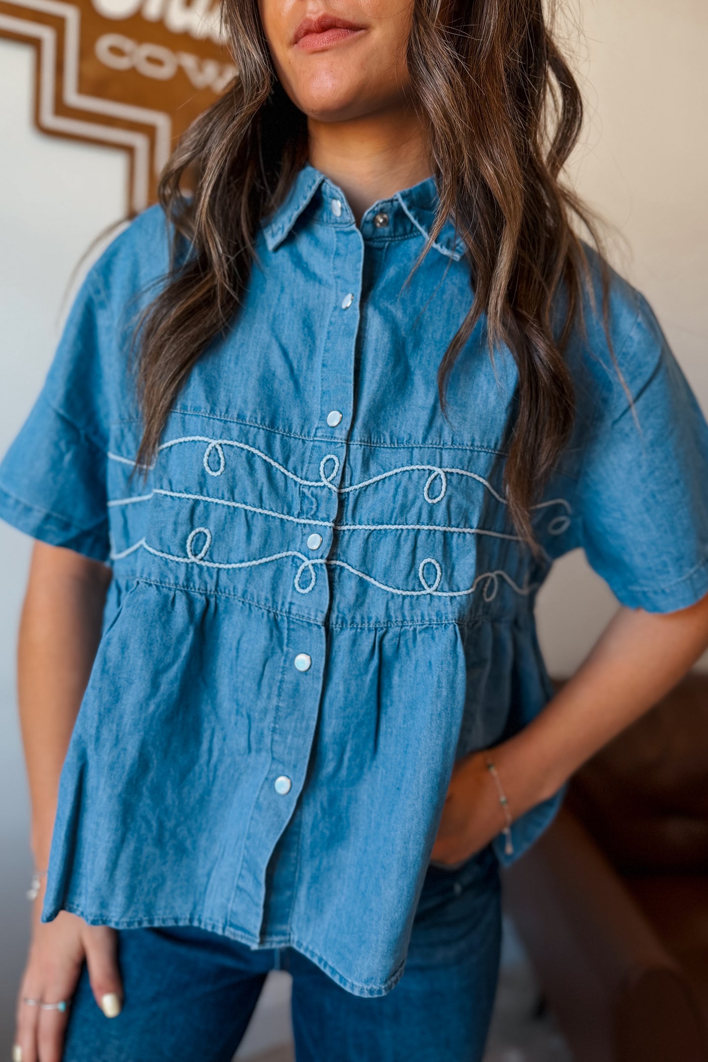 Light wash denim babydoll-style short sleeve top with pearl snap buttons and rope detailing at the front, relaxed fit for casual Western-inspired outfits