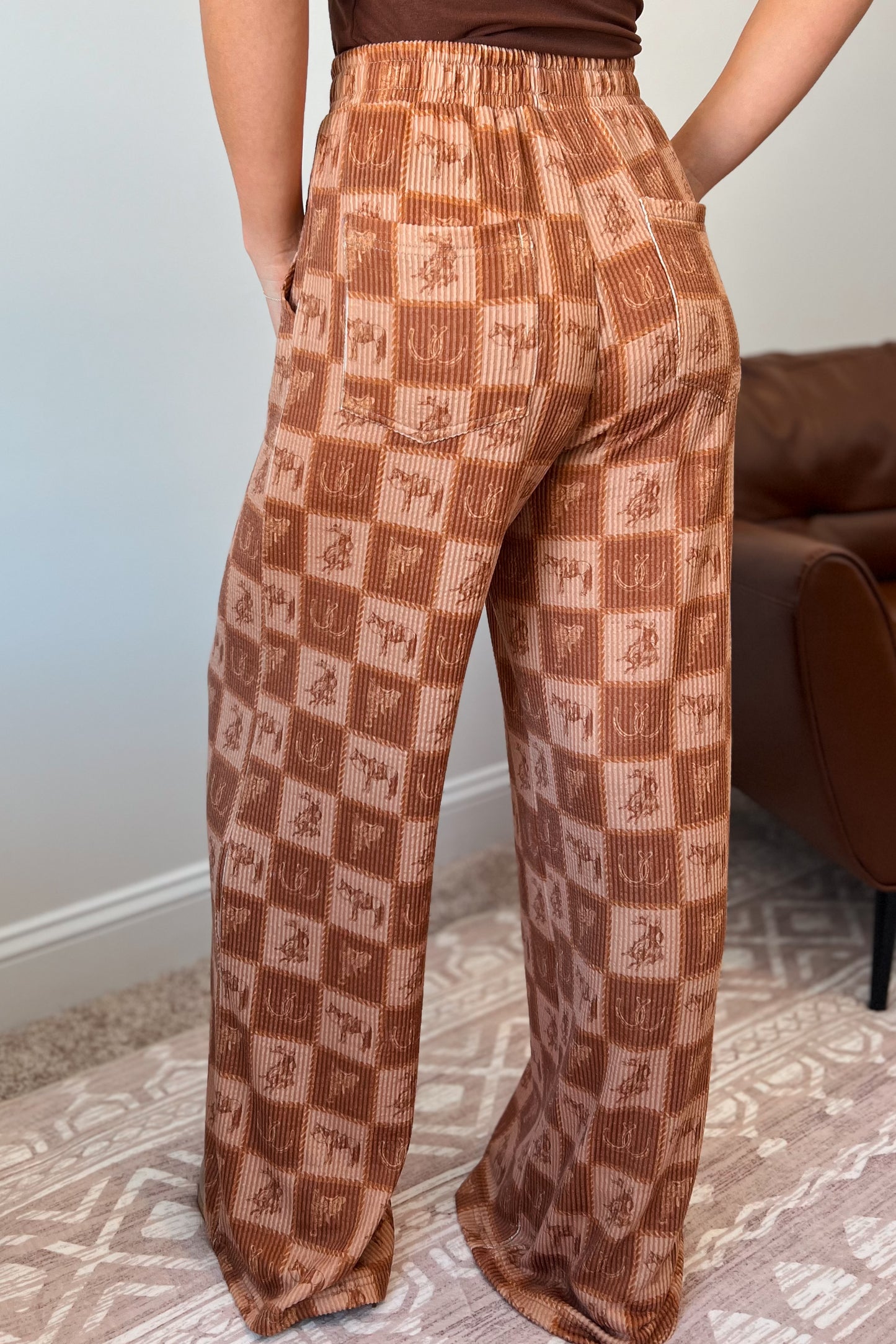 Brown wide-leg ribbed pants with elastic waistband, front pockets, and western checkered print featuring horses and horseshoes.