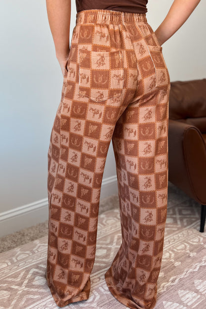 Brown wide-leg ribbed pants with elastic waistband, front pockets, and western checkered print featuring horses and horseshoes.