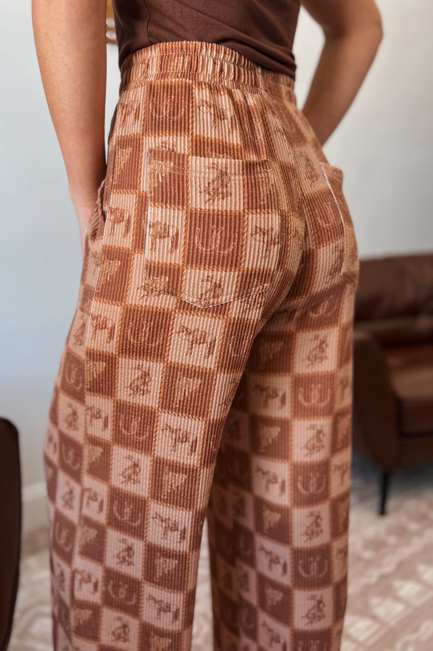 Brown wide-leg ribbed pants with elastic waistband, front pockets, and western checkered print featuring horses and horseshoes.
