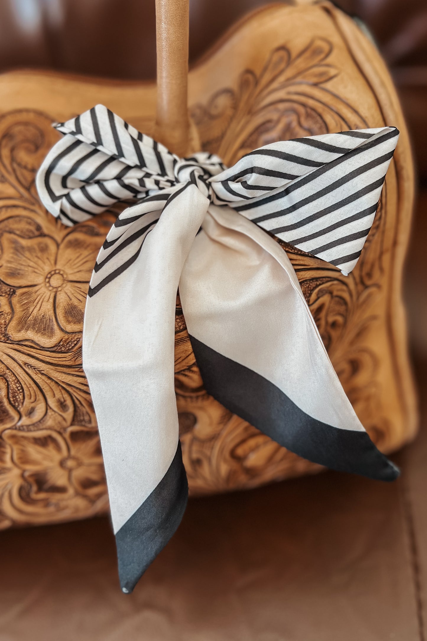 Black and white striped twilly scarf with solid ivory ends, tied around a tooled leather handbag strap