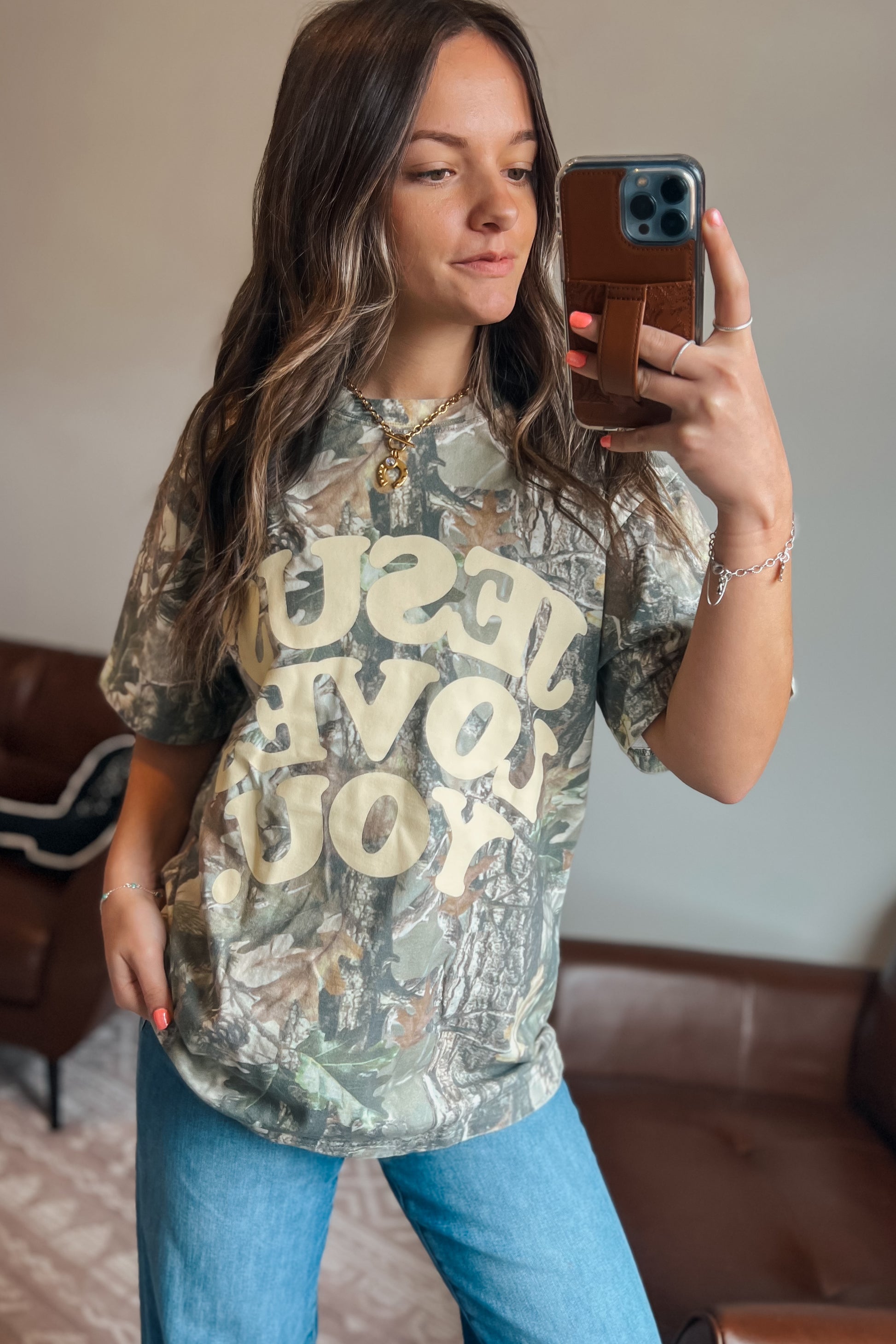 Model wearing oversized camouflage graphic t-shirt featuring “Jesus Loves You” text
