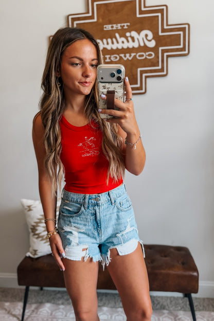 Model wearing high-rise light wash distressed denim cutoff shorts styled with a western-inspired outfit for a casual summer look.