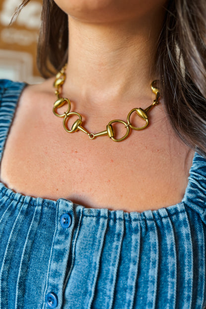 Close-up of gold short necklace featuring a snaffle bit design.