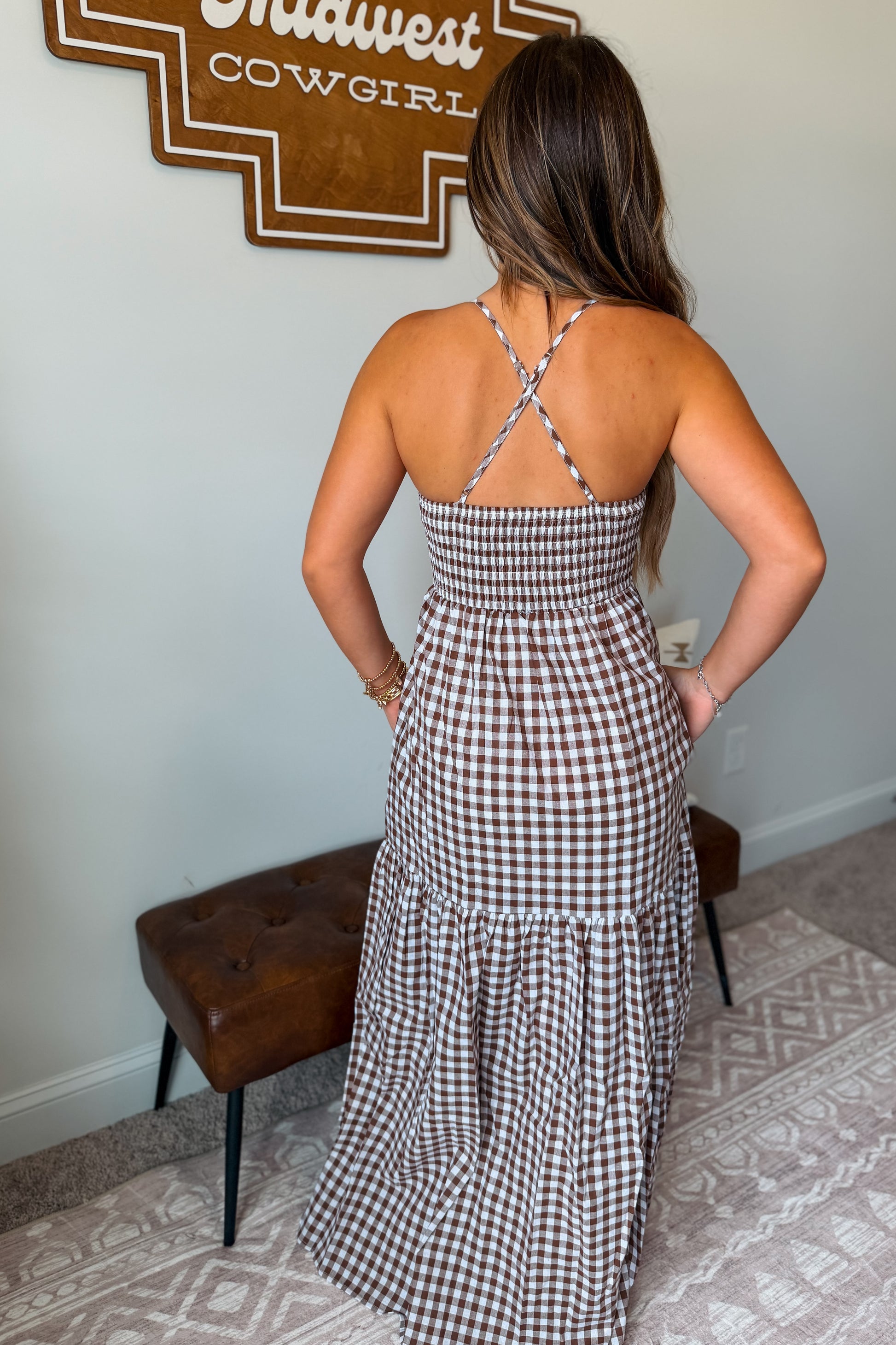Back view of a brown and white gingham maxi dress featuring crisscross spaghetti straps and a full-length skirt.