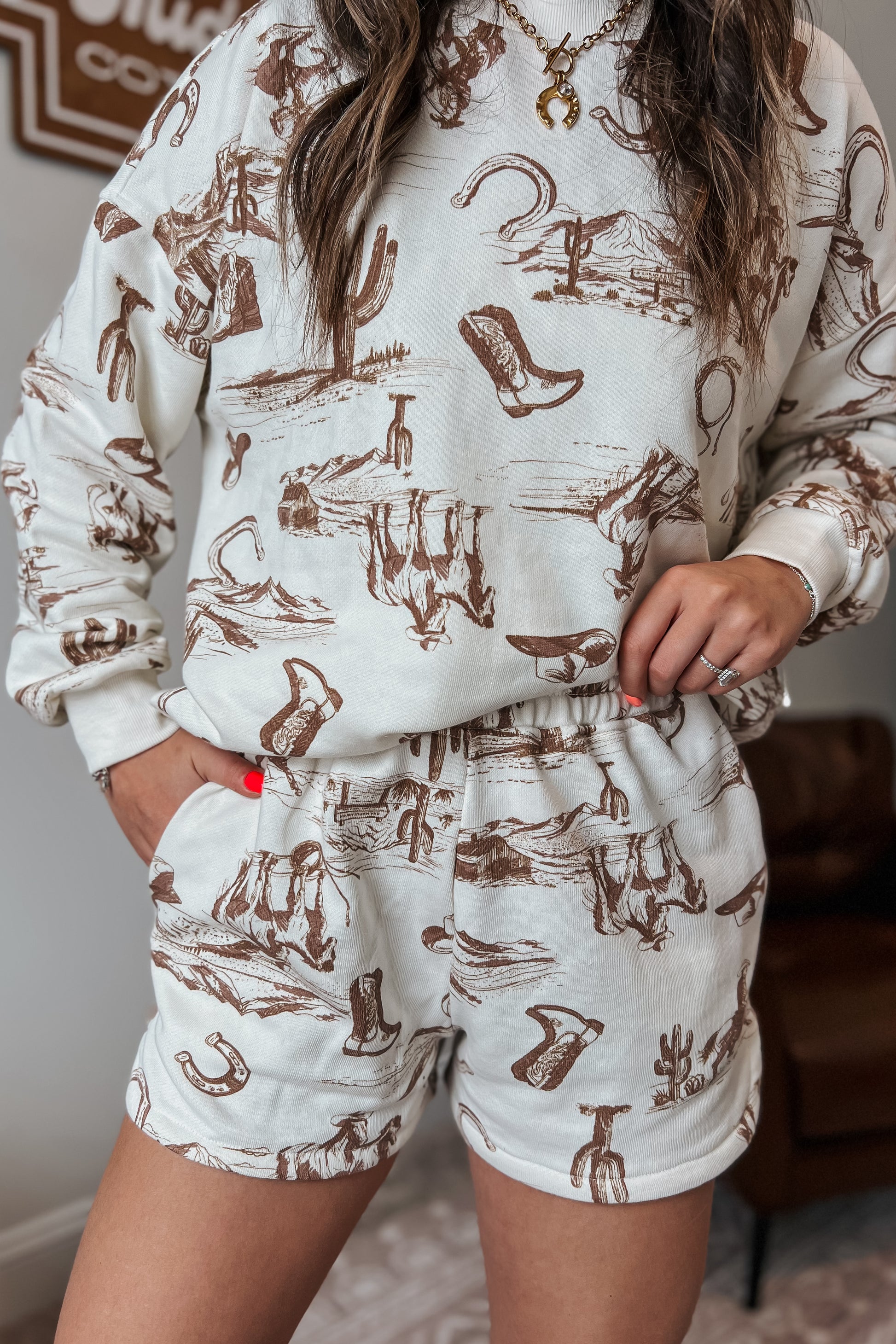 Cream elastic-waist shorts with brown western sketch print and side pockets.