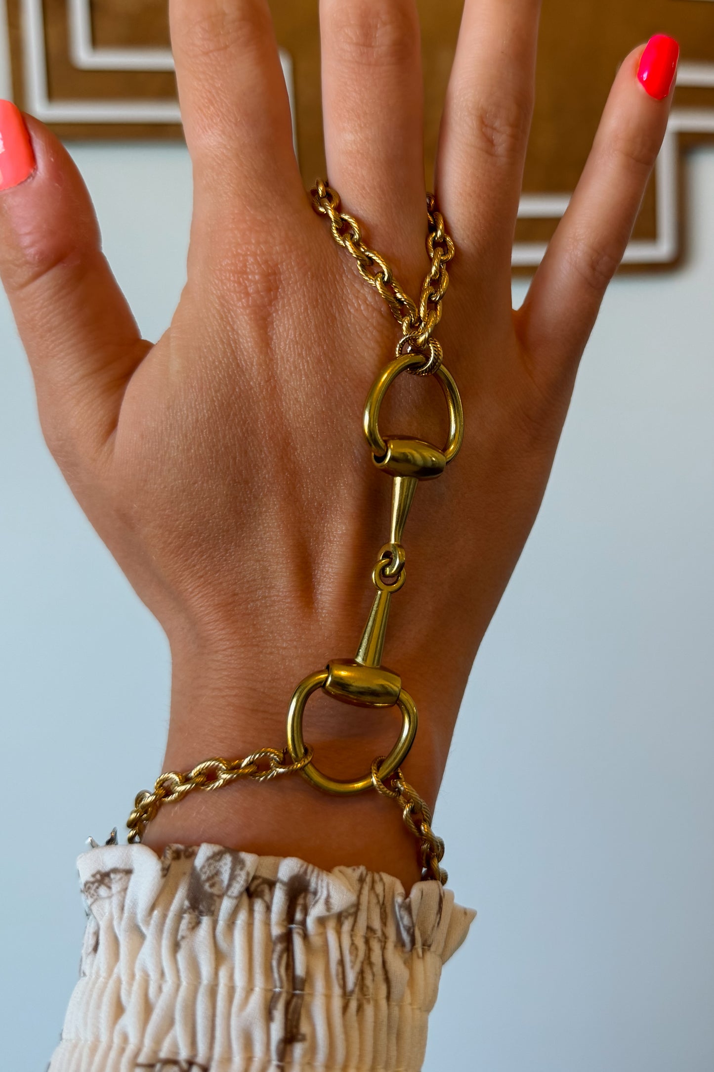 Front view of gold hand chain bracelet with snaffle bit detail connecting wrist and finger.