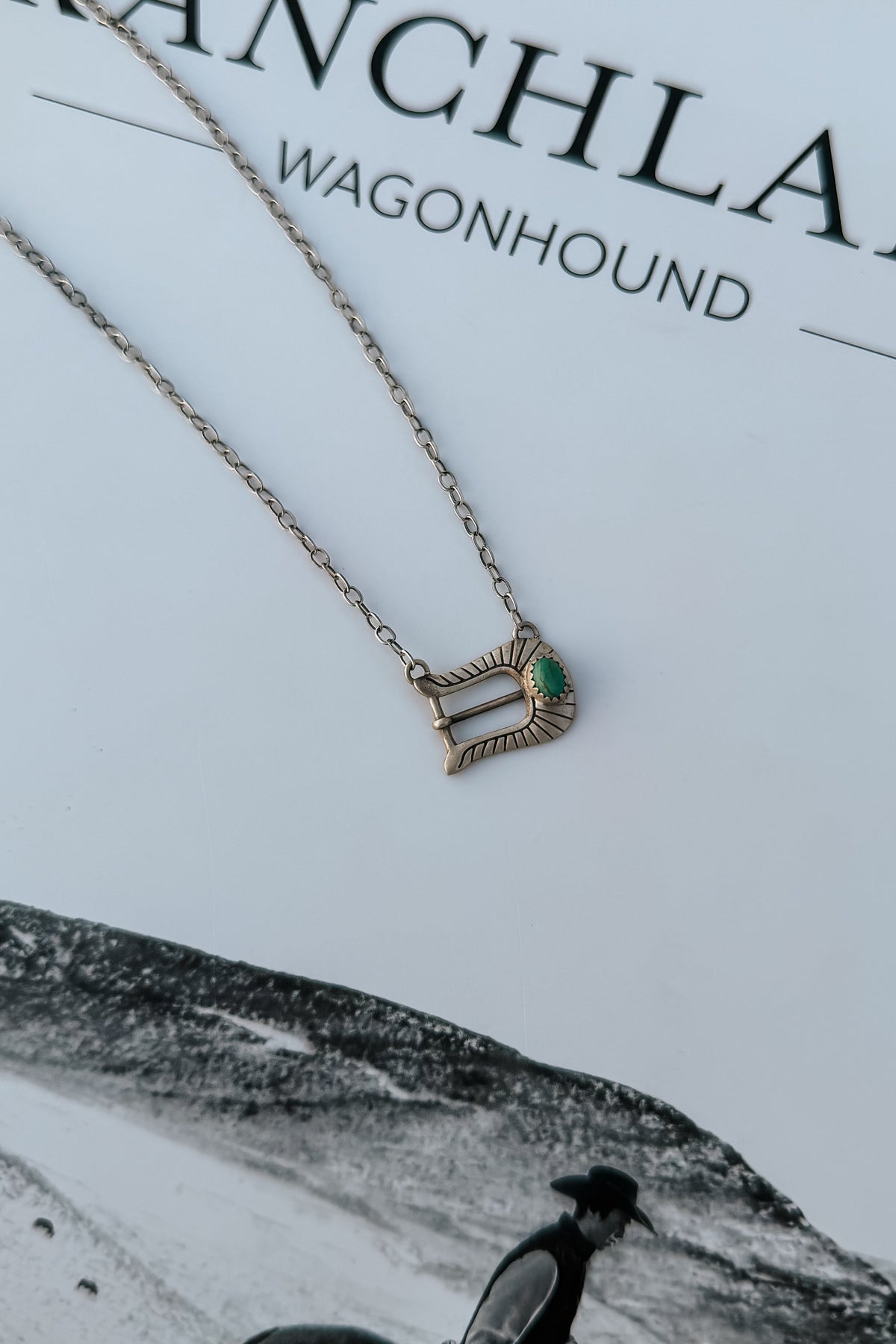 A delicate silver chain necklace with a small buckle pendant featuring a green stone accent, 