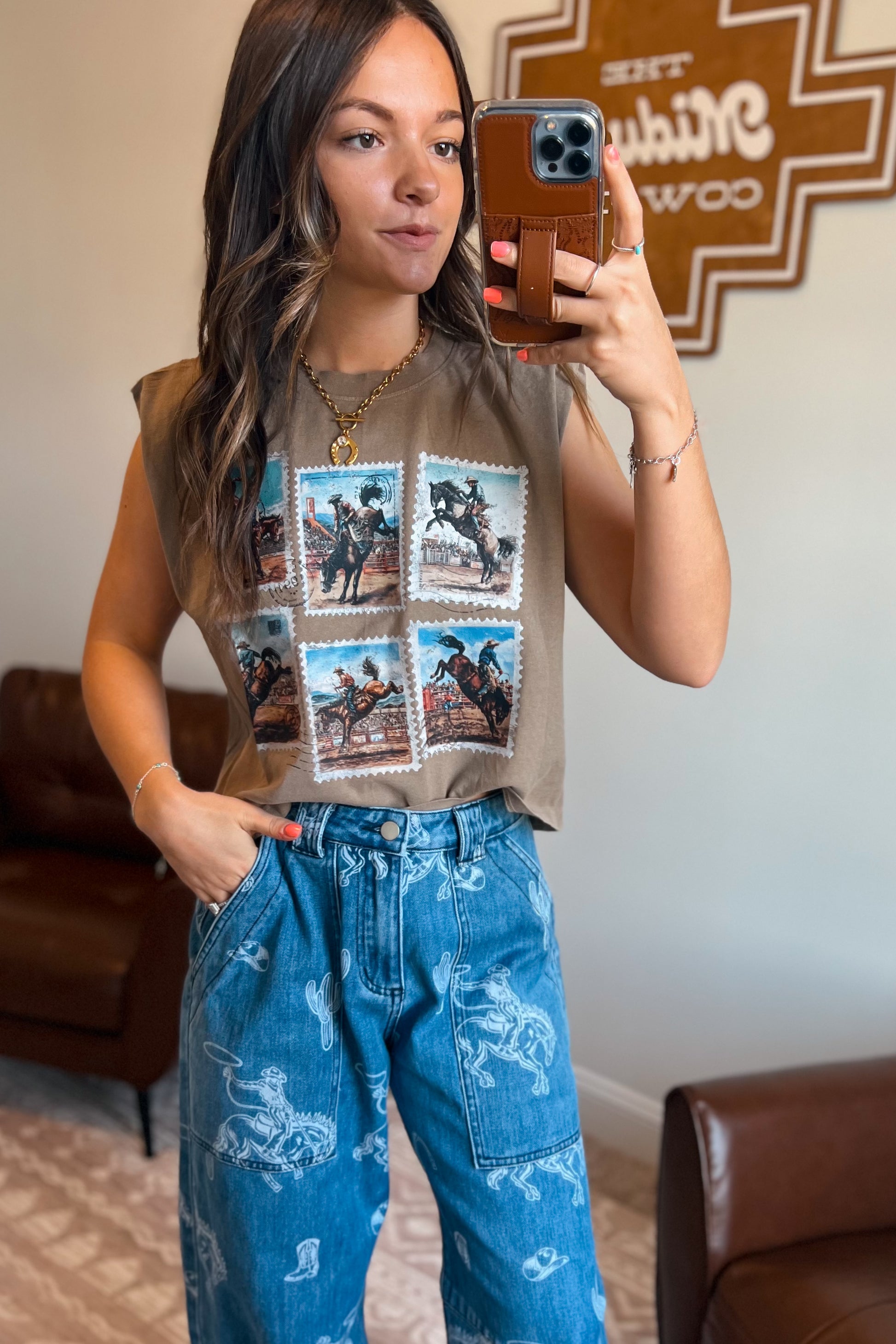 Brown sleeveless muscle tank featuring a vintage rodeo stamp graphic with six cowboy and bronc riding scenes, styled with blue western-print jeans.