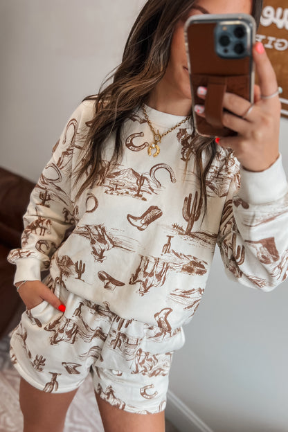 Cream long-sleeve sweatshirt with brown western sketch print, paired with matching elastic-waist shorts with side pockets.