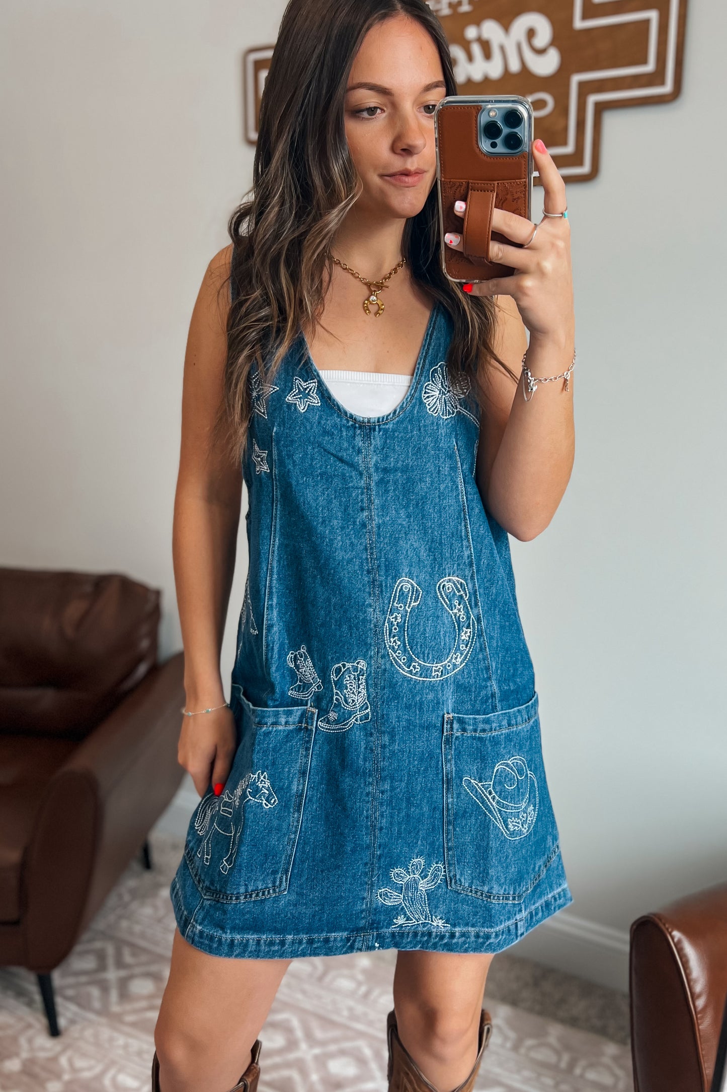 Blue denim overall dress with adjustable shoulder straps, white western embroidery, and two front patch pockets.