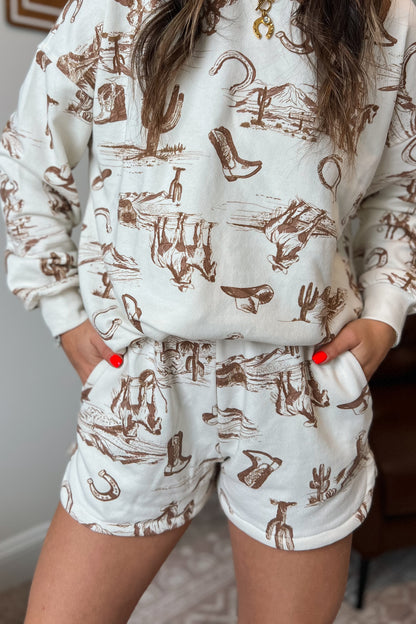 Cream elastic-waist shorts with brown western sketch print and side pockets.