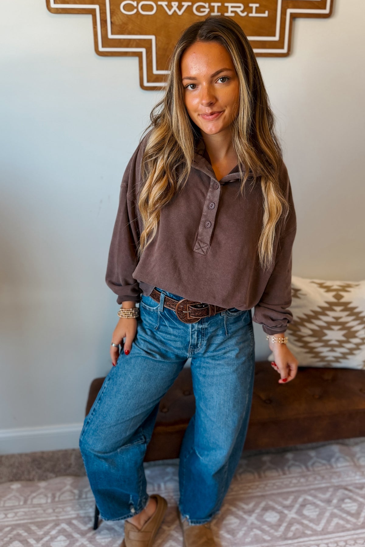 A woman wearing a brown long-sleeve brown top and blue jeans, 