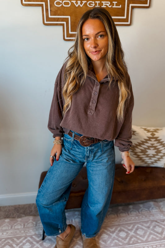 A woman wearing a brown long-sleeve brown top and blue jeans, 