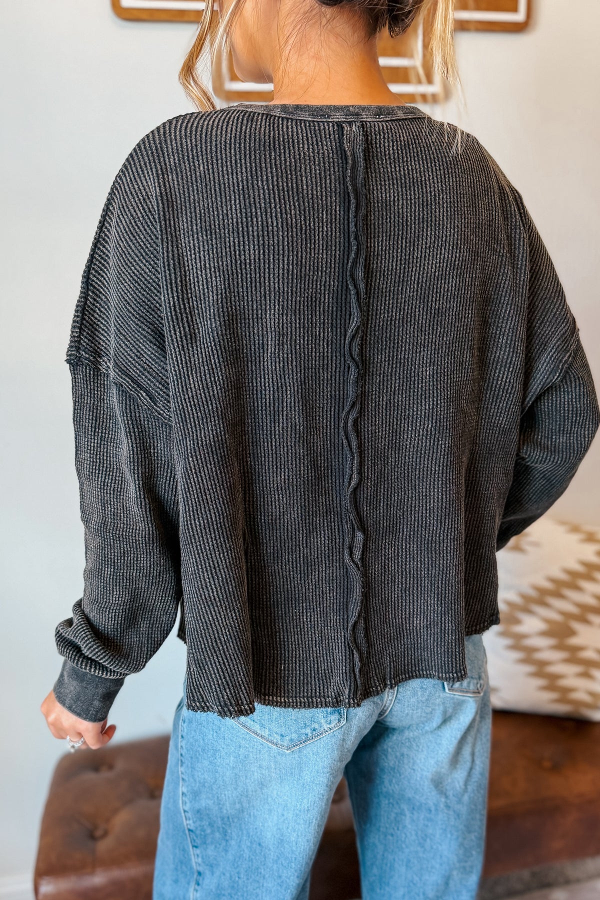 A person shown from the back wearing a dark charcoal gray ribbed knit sweater with a distinctive wavy vertical seam down the center back, paired with light blue jeans.