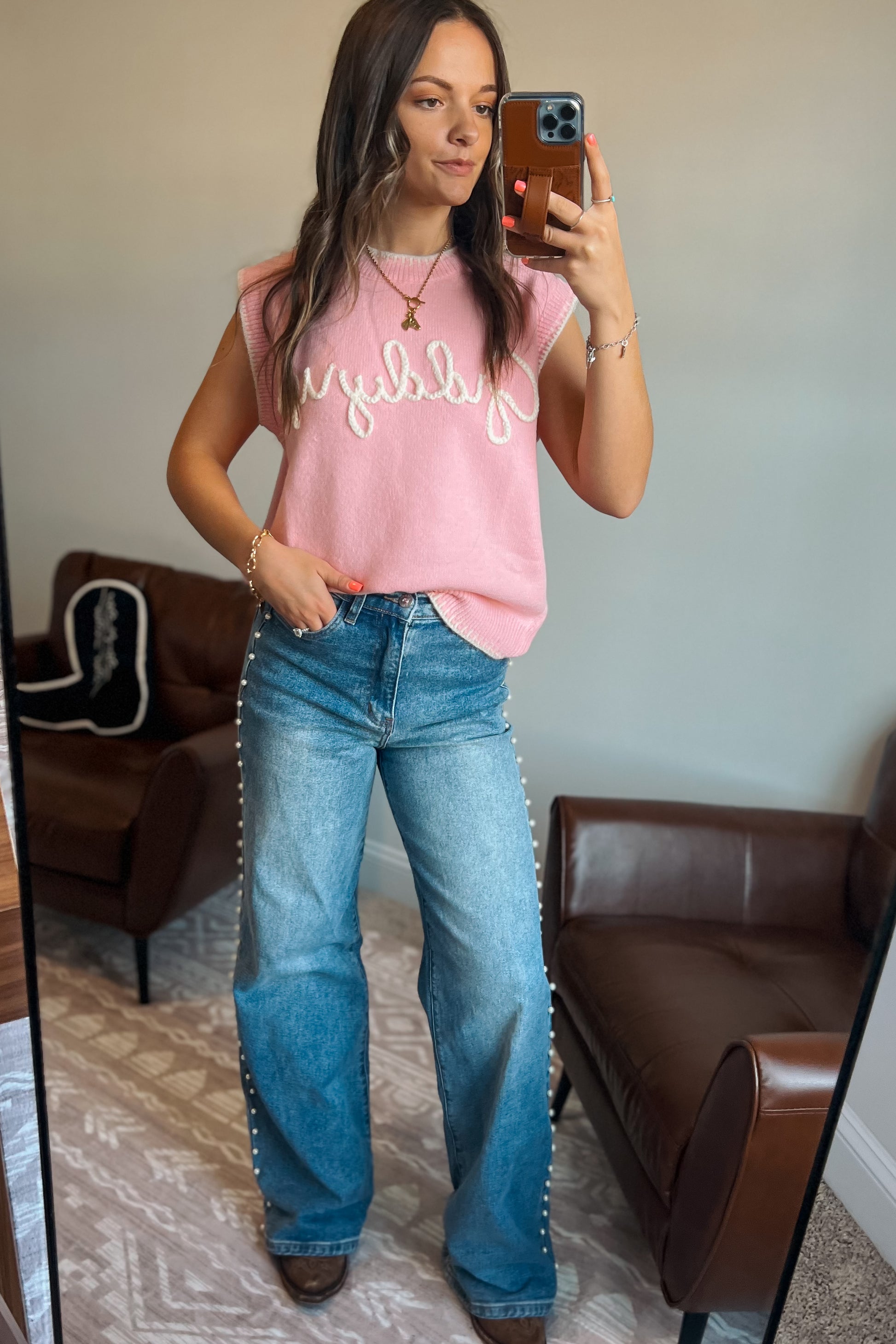 Model wearing pink knit sweater vest with “Giddy Up” text and light wash jeans with pearls