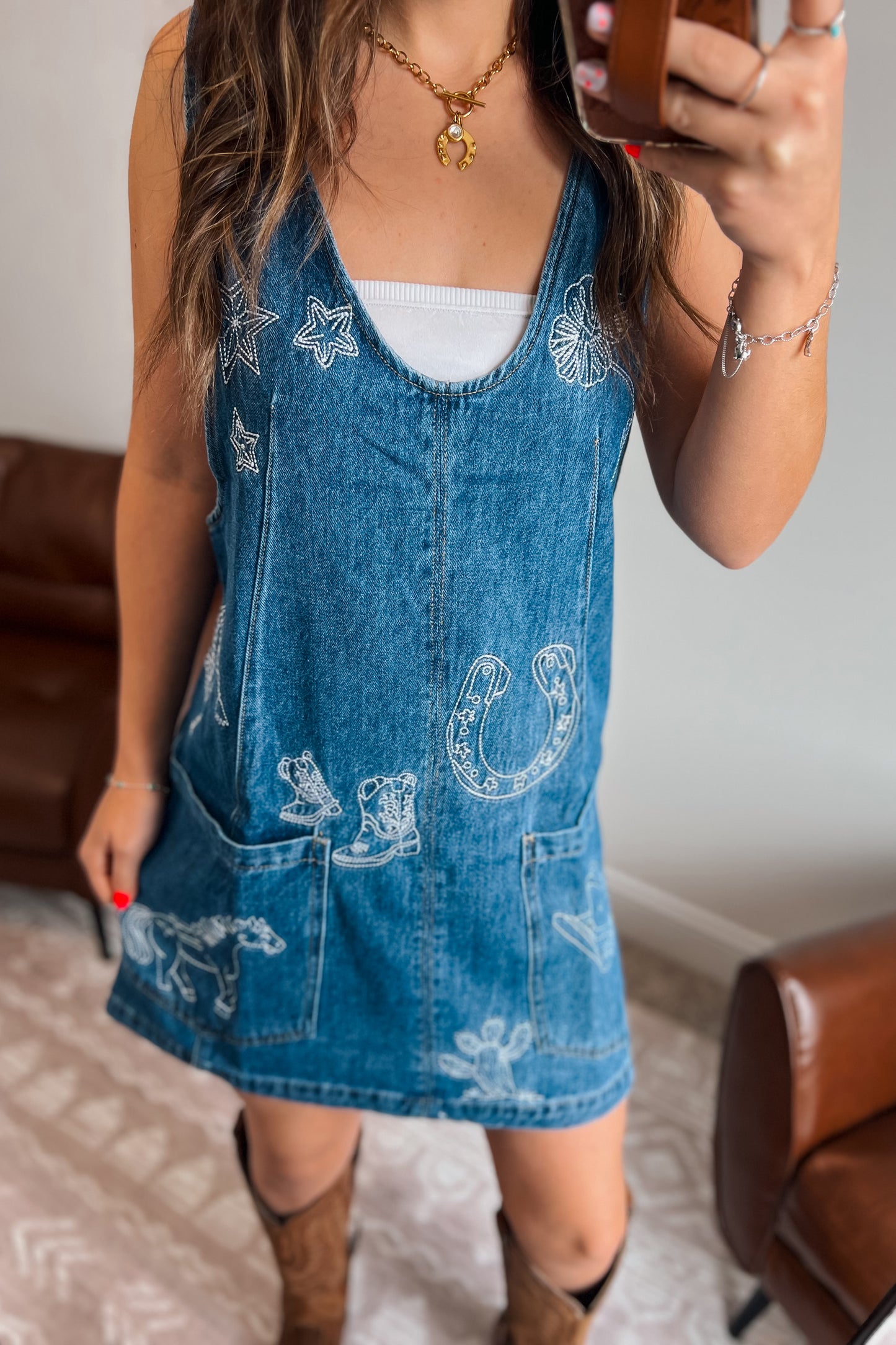 Blue denim overall dress with adjustable shoulder straps, white western embroidery, and two front patch pockets.