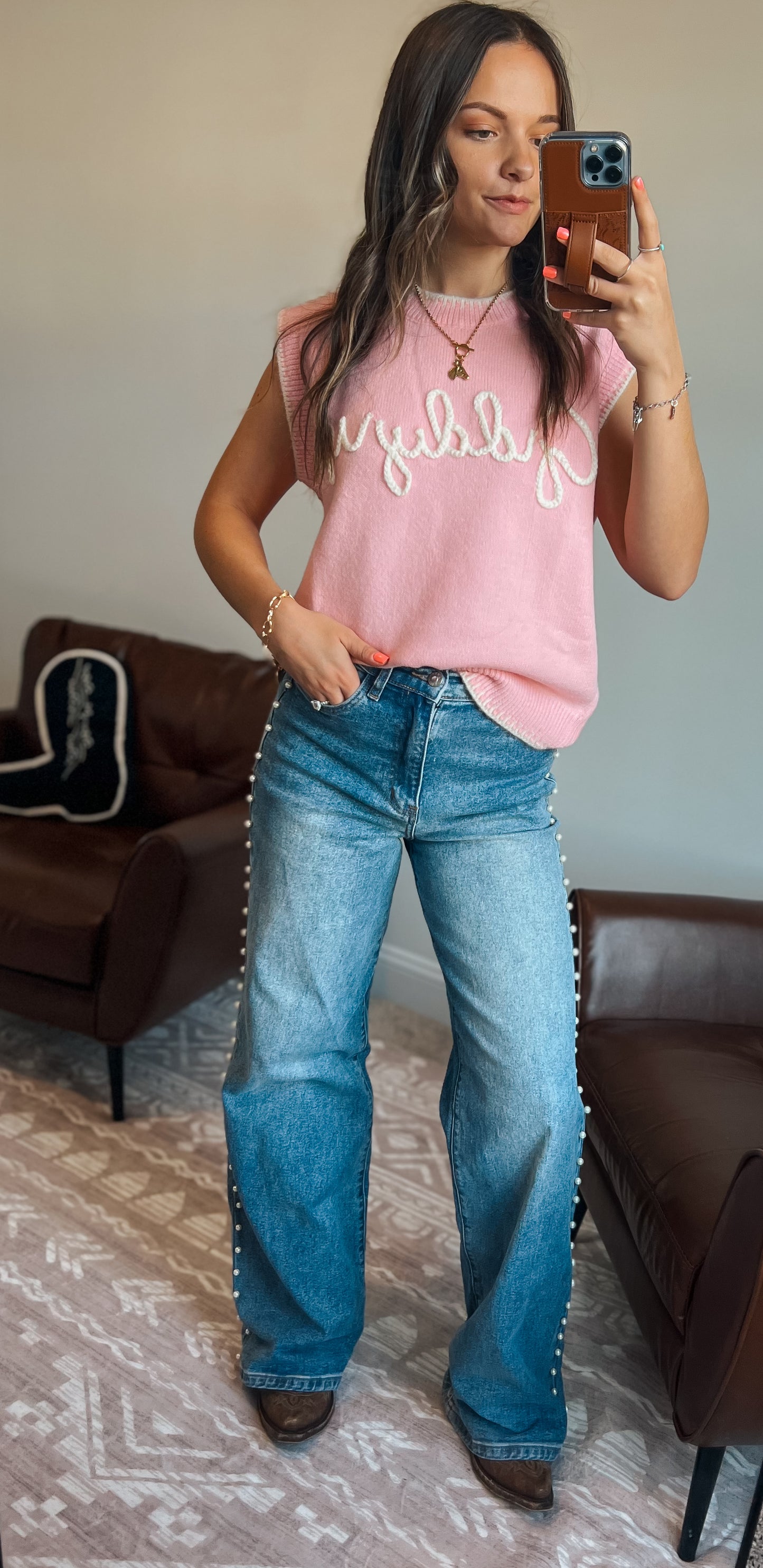 Model wearing pink knit sweater vest with “Giddy Up” text and wide leg denim jeans with pearl detailing