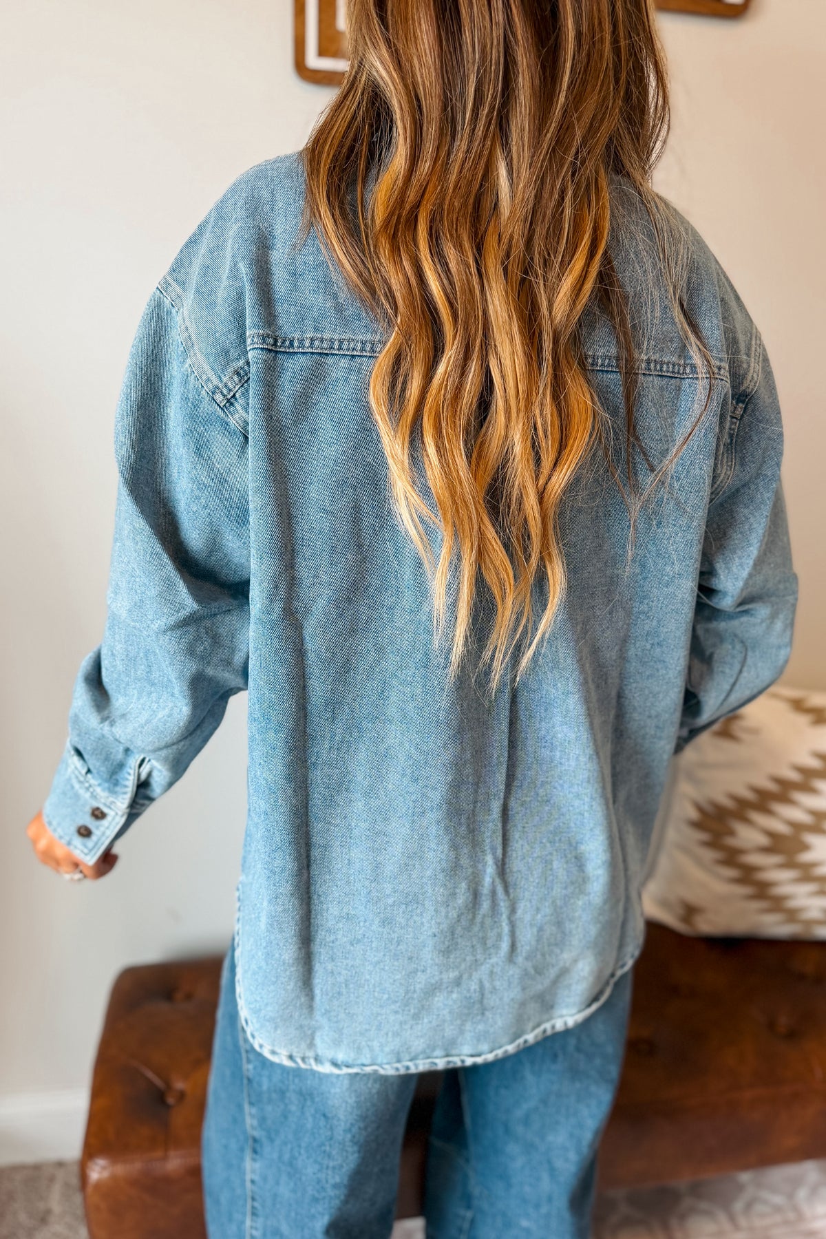 A person shown from behind wearing an oversized light blue denim shirt and blue jeans in a home setting.