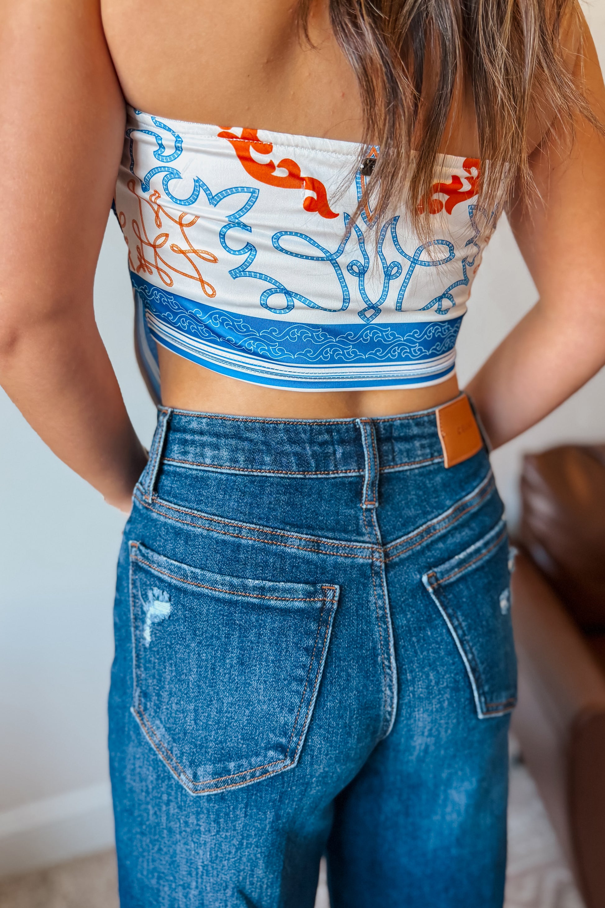 Back view Model wearing a white strapless tube top with blue and orange western print.