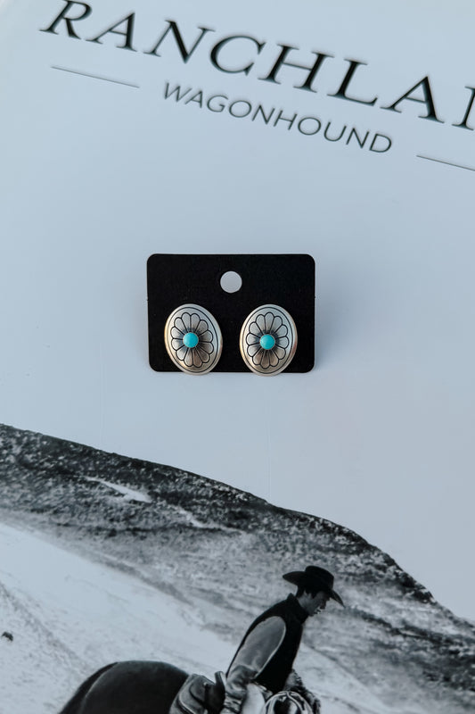 Silver-toned oval stud earrings with turquoise centers and floral detailing, displayed on a black card against a white background