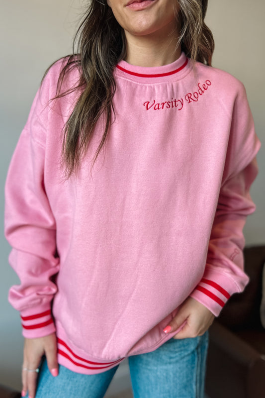 Model wearing pink western-inspired sweatshirt with “Varsity Rodeo” embroidery and red striped trim
