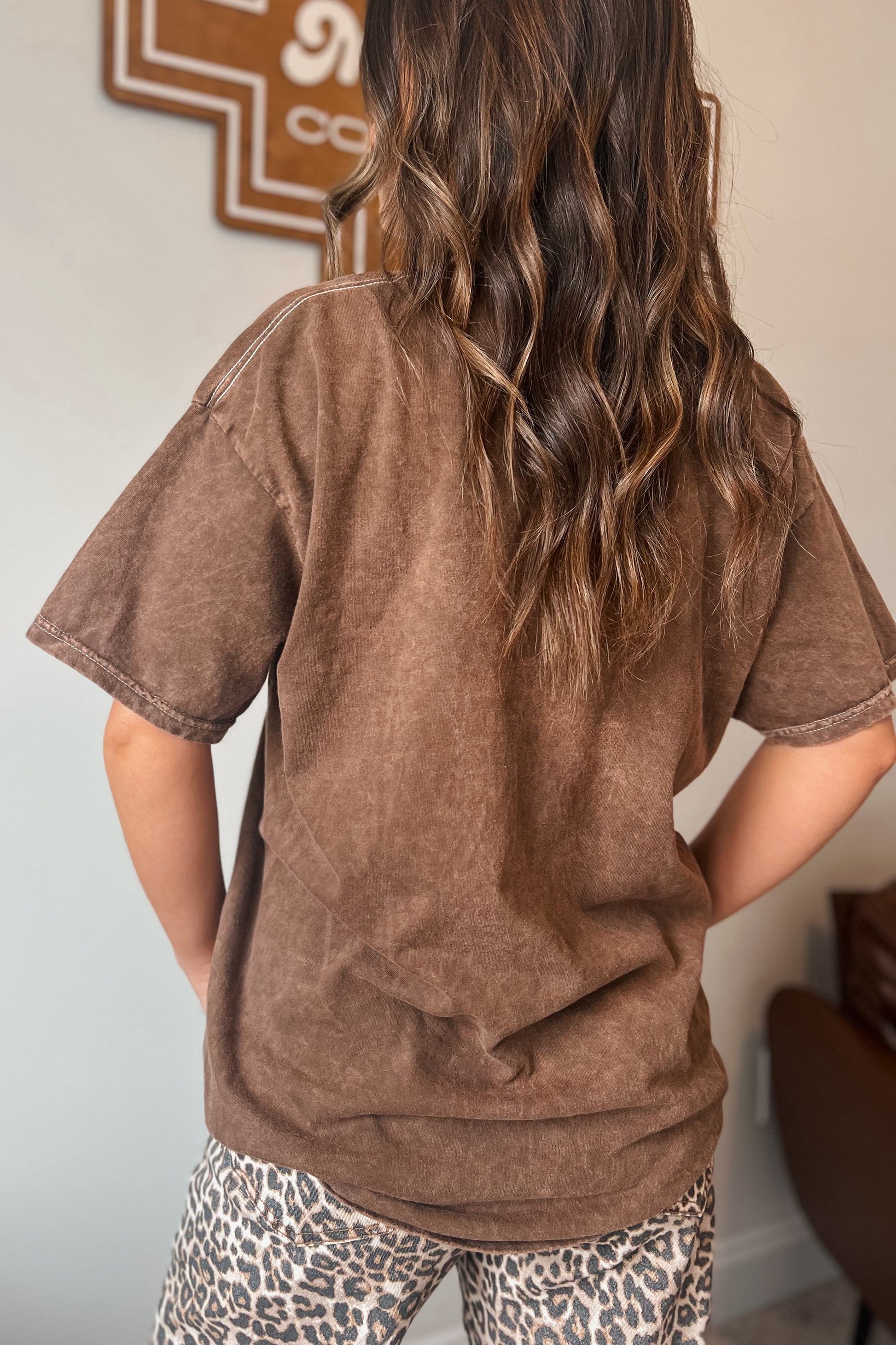 Back view of brown vintage-wash short sleeve graphic tee paired with leopard print bottoms.