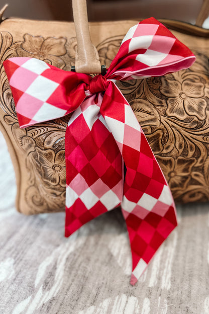 Pink and red diamond print twilly scarf tied in a bow on a tooled leather handbag 
