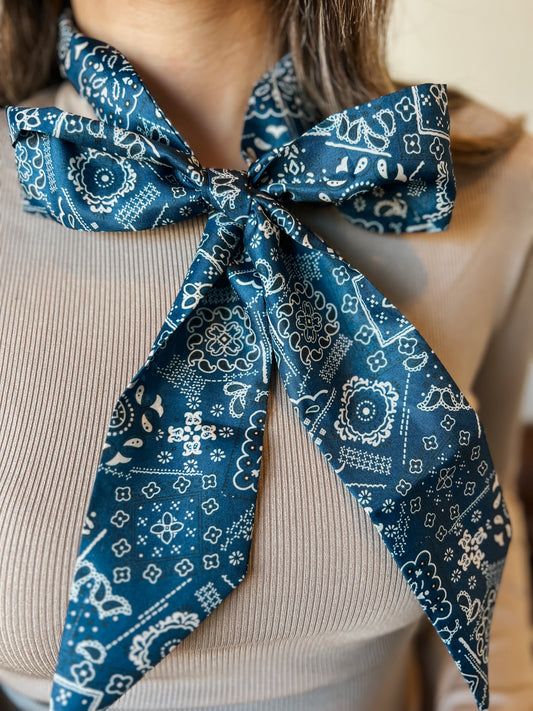 Close-up of a blue paisley twilly tied around the neck, featuring a white western-inspired print and pointed ends.