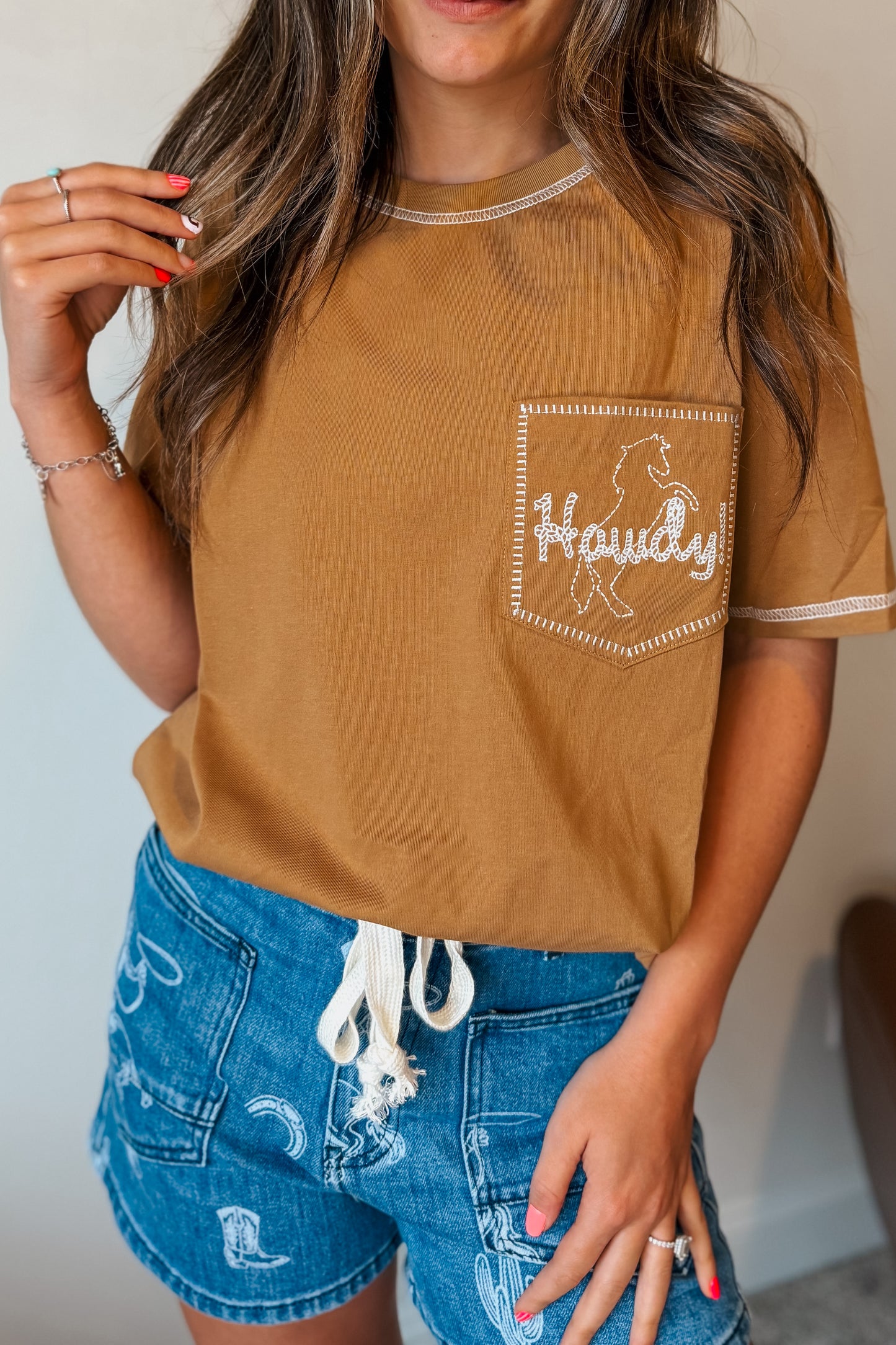 Camel colored short sleeve tee with a front chest pocket embroidered with the word “Howdy.”