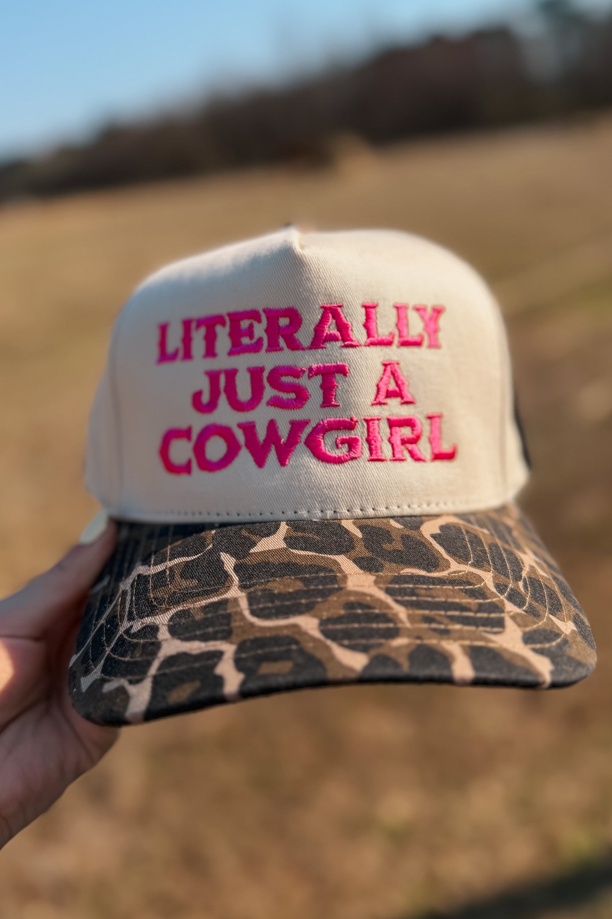 Trucker hat with hot pink “Literally Just a Cowgirl” embroidery and cheetah print brim.