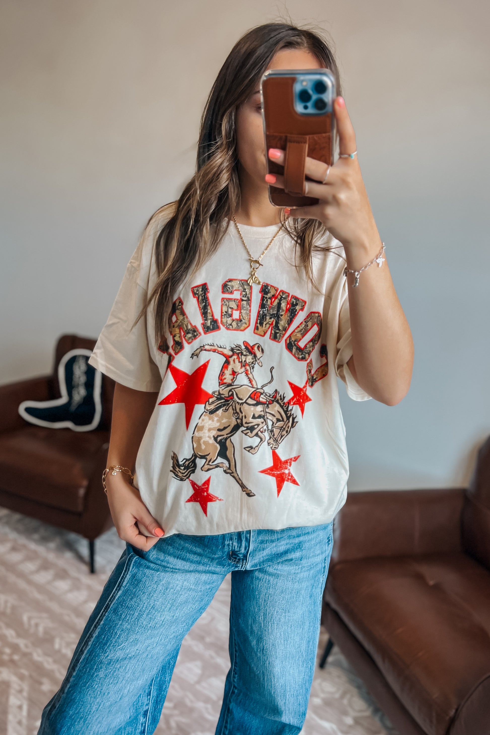 Close-up of oversized western graphic t-shirt featuring “Cowgirl” text, cowboy rider illustration, and red star details
