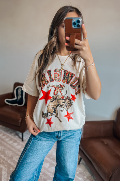 Close-up of oversized western graphic t-shirt featuring “Cowgirl” text, cowboy rider illustration, and red star details
