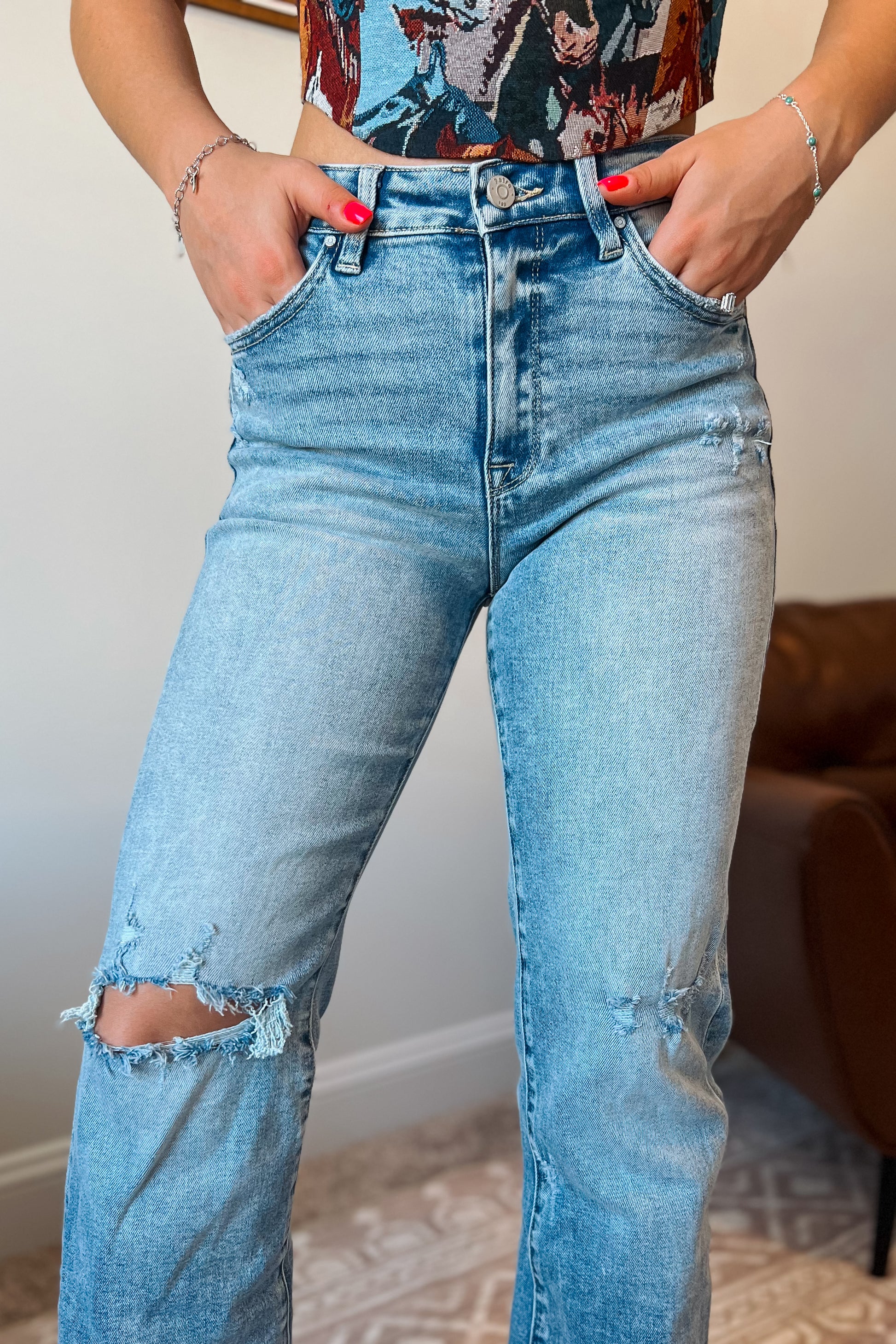 Close-up of light wash denim jeans showing button closure, zipper fly, and front pockets.