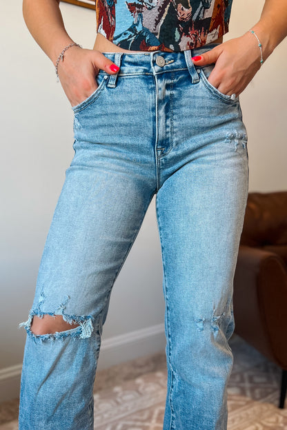 Close-up of light wash denim jeans showing button closure, zipper fly, and front pockets.