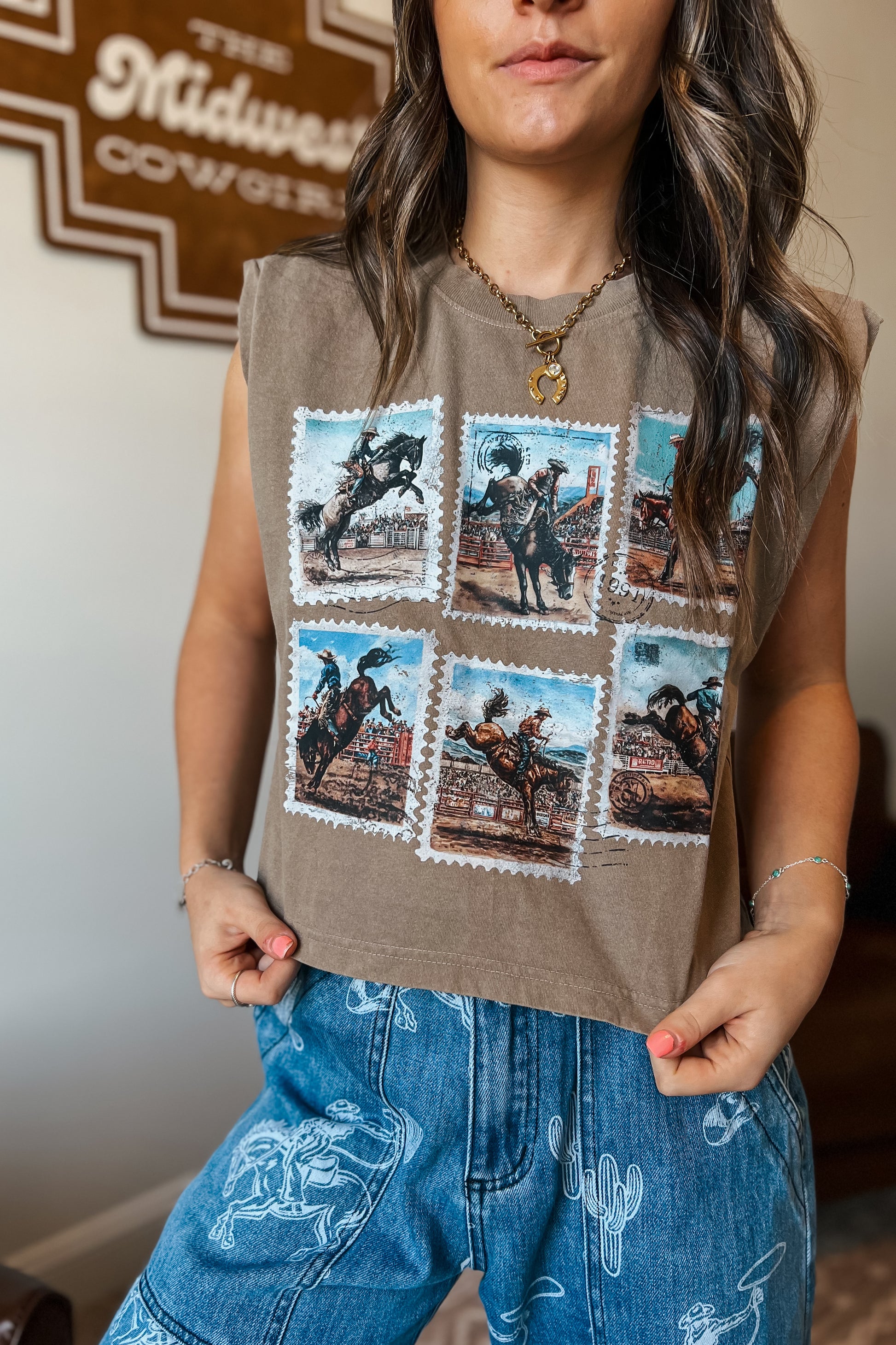Brown sleeveless muscle tank featuring a vintage rodeo stamp graphic with six cowboy and bronc riding scenes, styled with blue western-print jeans.