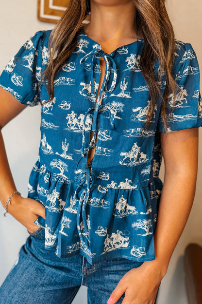 Blue puff sleeve babydoll top with white western print and front tie detail.